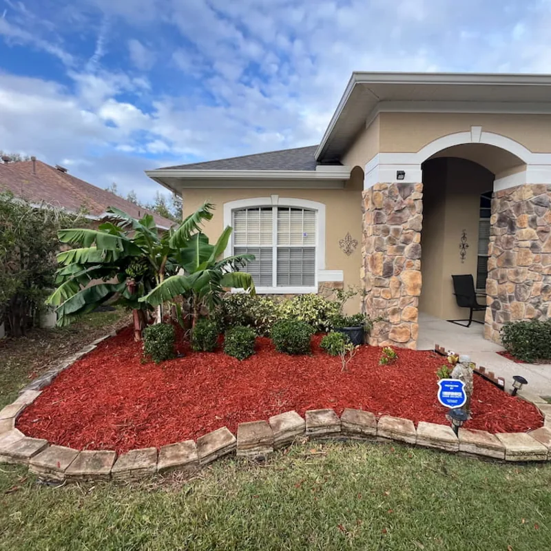 Curved front bed with red mulch, stone edging and tropical planting